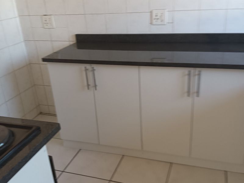 A functional kitchen area featuring white cabinetry, dark granite countertops, and tiled surfaces, offering a clean and practical space for culinary activities.