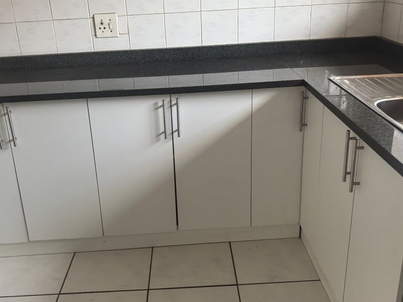 A functional kitchen featuring white cabinetry, dark granite countertops, a stainless steel sink, and tiled flooring with a matching backsplash.