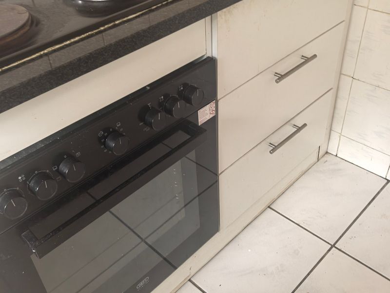 A functional kitchen area featuring a built-in oven, electric hob, granite countertops, and tiled finishes throughout.