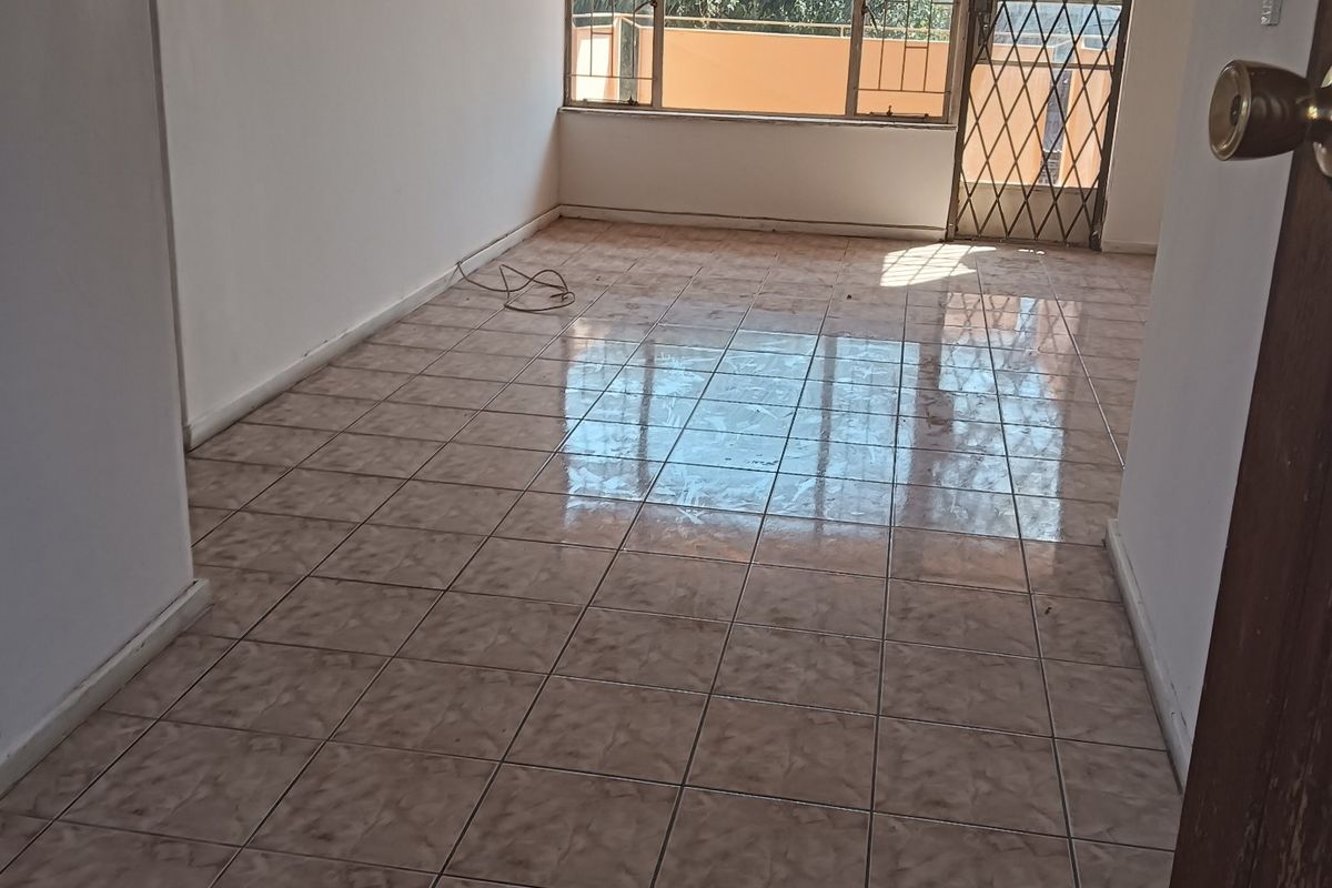 An empty, tiled living room featuring a security gate and large window, offering a blank canvas for potential renovation and interior design.