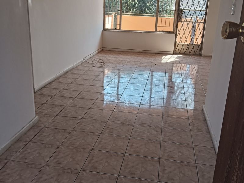 An empty, tiled living room featuring a security gate and large window, offering a blank canvas for potential renovation and interior design.