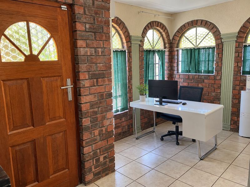 A home office featuring distinctive exposed brick walls, arched windows, and tiled flooring, providing a unique and characterful workspace.