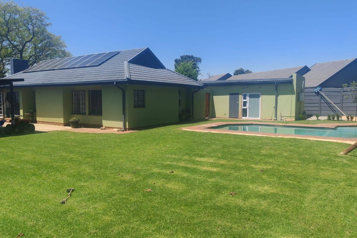 Rear view of the property featuring a well-maintained lawn, a swimming pool, and a house exterior equipped with solar panels on the roof.