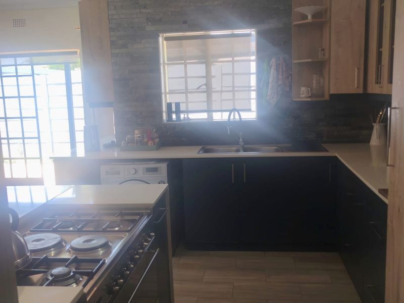 Modern kitchen featuring dark cabinetry, stone countertops, a gas hob, and a distinctive stone veneer splashback with integrated sink.