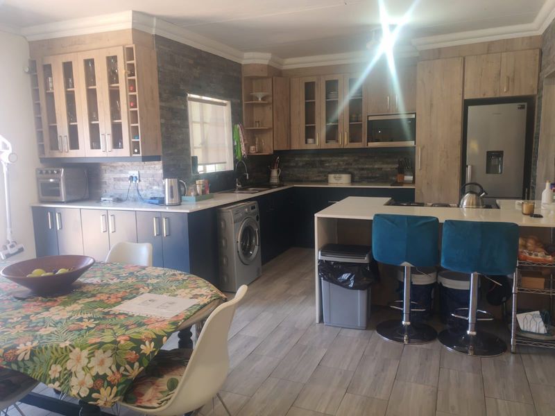 Open plan kitchen and dining area featuring modern wood-look cabinetry, stone veneer backsplash, and a functional kitchen island with breakfast bar seating.