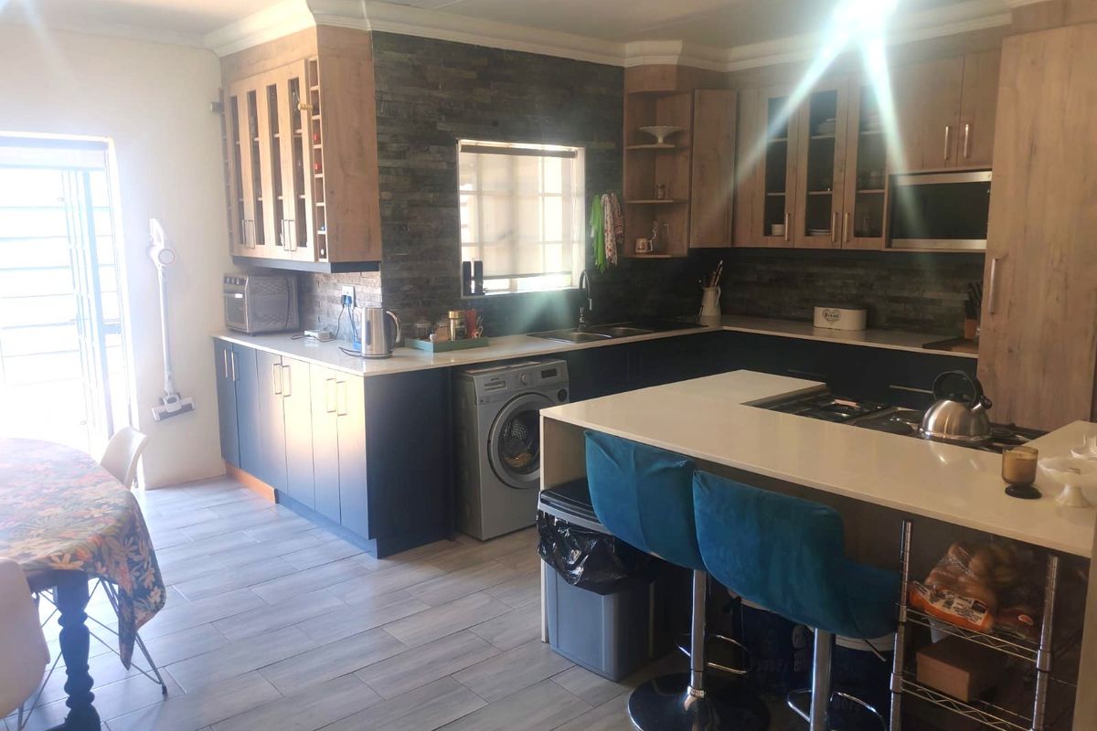Modern kitchen featuring two-tone cabinetry, stone veneer backsplash, stone countertops, and a functional island with integrated hob, complemented by tiled flooring.