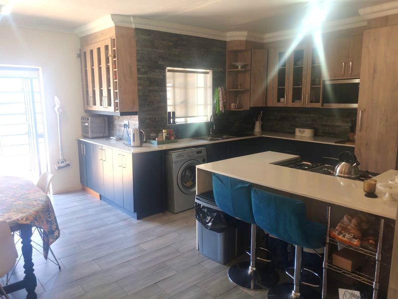 Modern kitchen featuring two-tone cabinetry, stone veneer backsplash, stone countertops, and a functional island with integrated hob, complemented by tiled flooring.