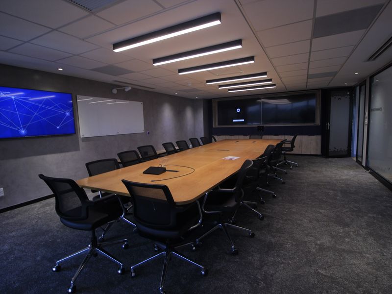 Modern professional boardroom featuring integrated display screens, linear lighting, glass partitions, and high-quality finishes suitable for corporate meetings.