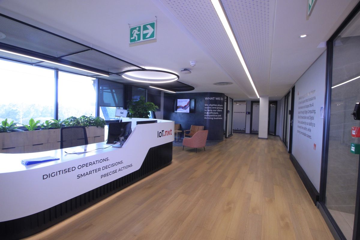 Modern commercial reception area featuring a sleek built-in desk, timber flooring, recessed linear lighting, and large windows providing ample natural light.