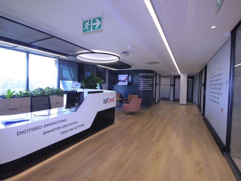 Modern commercial reception area featuring a sleek built-in desk, timber flooring, recessed linear lighting, and large windows providing ample natural light.