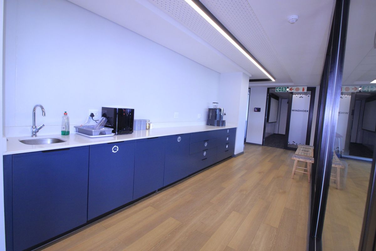Modern commercial kitchenette featuring sleek blue cabinetry, white countertops, integrated sink, and high-quality wood-look flooring in a professional office environment.