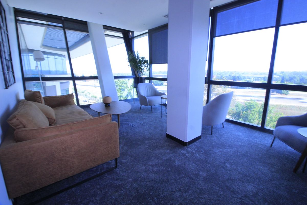 Modern commercial lounge area featuring expansive floor-to-ceiling windows with panoramic views, structural columns, and high-quality carpeted flooring.