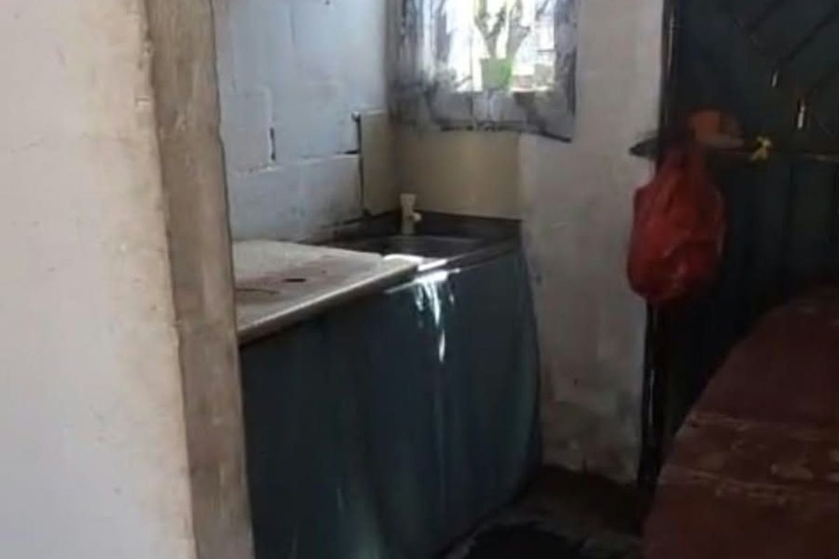 A compact scullery area featuring a sink, built-in shelving, and a window, requiring significant renovation to improve the wall and floor finishes.