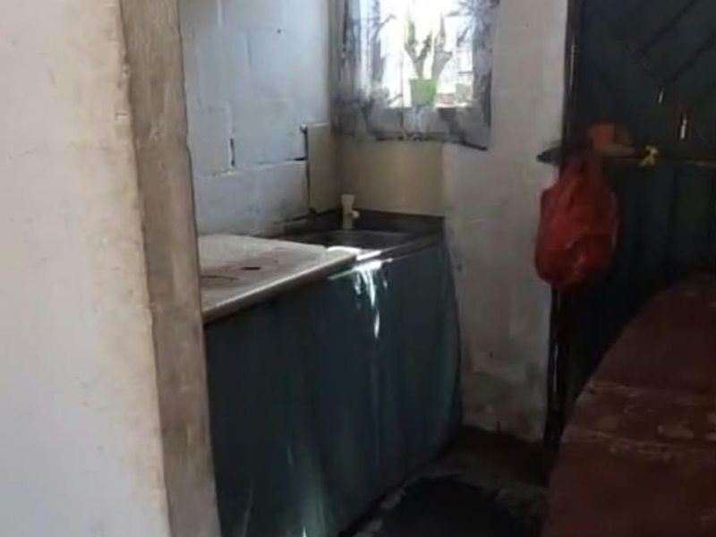 A compact scullery area featuring a sink, built-in shelving, and a window, requiring significant renovation to improve the wall and floor finishes.