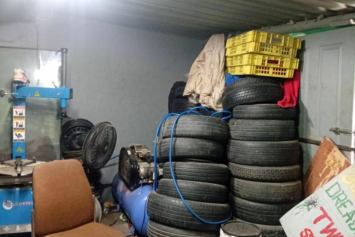A cluttered garage space featuring a tyre changing machine and corrugated metal ceiling, currently used for storage and automotive maintenance.