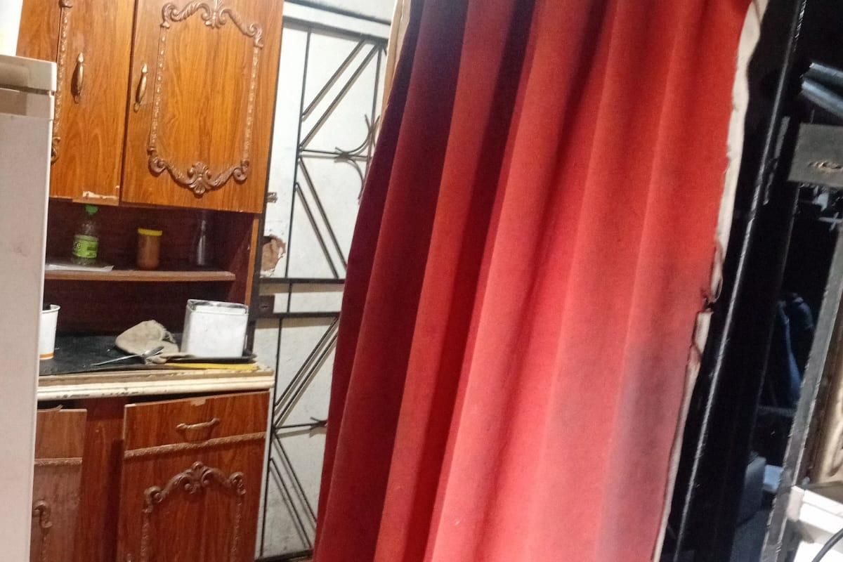 A small kitchen area featuring traditional wooden cabinetry, tiled flooring, and a security gate, currently showing signs of wear and dated finishes.