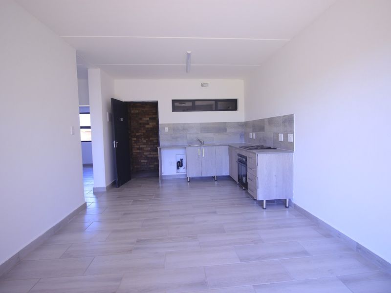 An open-plan living and kitchen area featuring modern light-wood cabinetry, built-in oven, hob, and neutral tiled flooring throughout.