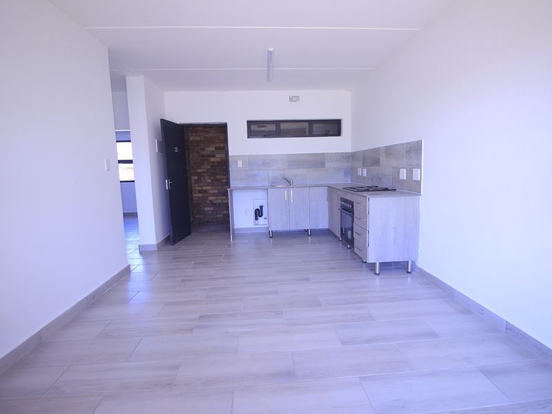 An open-plan living and kitchen area featuring modern tiled flooring, built-in cabinetry, and a functional kitchen layout with a built-in oven and hob.