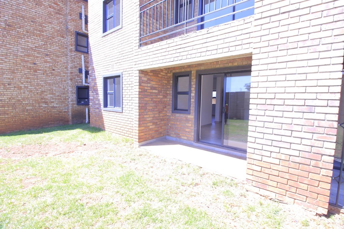 Rear view of the apartment building featuring a face brick facade, a ground-level concrete patio, and a sliding glass door leading to the interior.