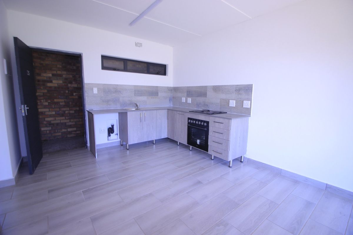 A clean, modern kitchen featuring light wood-finish cabinetry, built-in oven and hob, tiled backsplash, and neutral floor tiles in an open-plan layout.