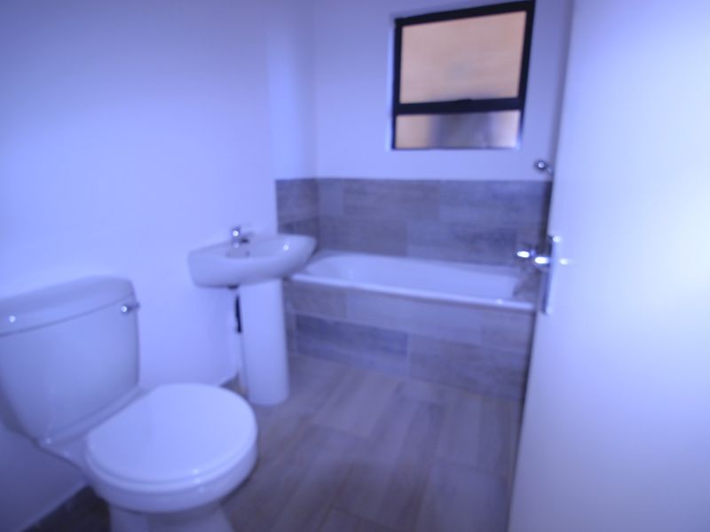 A clean, modern bathroom featuring a pedestal basin, toilet, and a bathtub with tiled splashback.