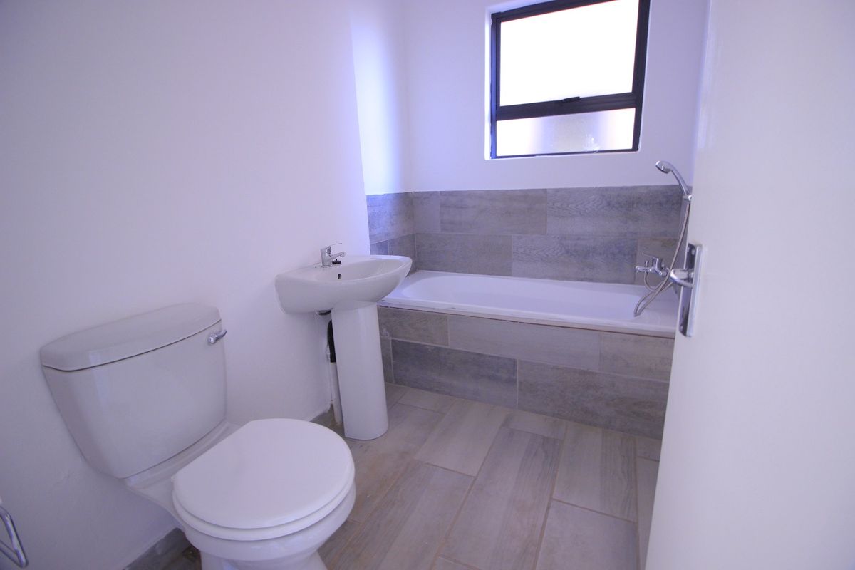 A clean and modern bathroom featuring a pedestal basin, toilet, and a bathtub with tiled surround and flooring.