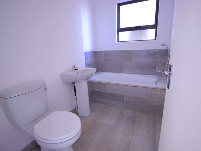 A clean and modern bathroom featuring a pedestal basin, toilet, and a bathtub with tiled surround and flooring.