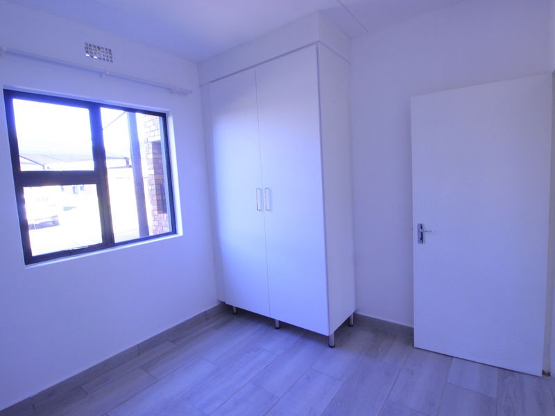 A bright, empty bedroom featuring modern tiled flooring, a built-in wardrobe, and an aluminium-framed window.