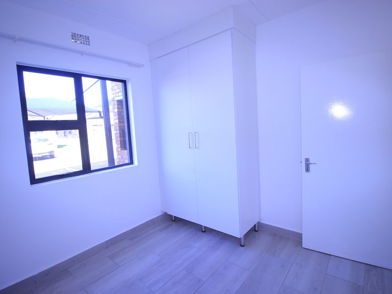 A clean, empty bedroom featuring modern tiled flooring, a built-in wardrobe, and an aluminium-framed window.