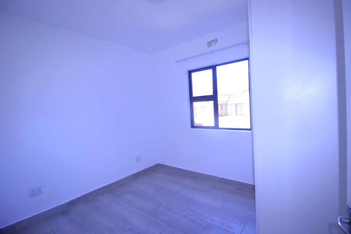 A clean, empty bedroom featuring neutral tiled flooring and a modern aluminium window frame, providing a blank canvas for personalization.