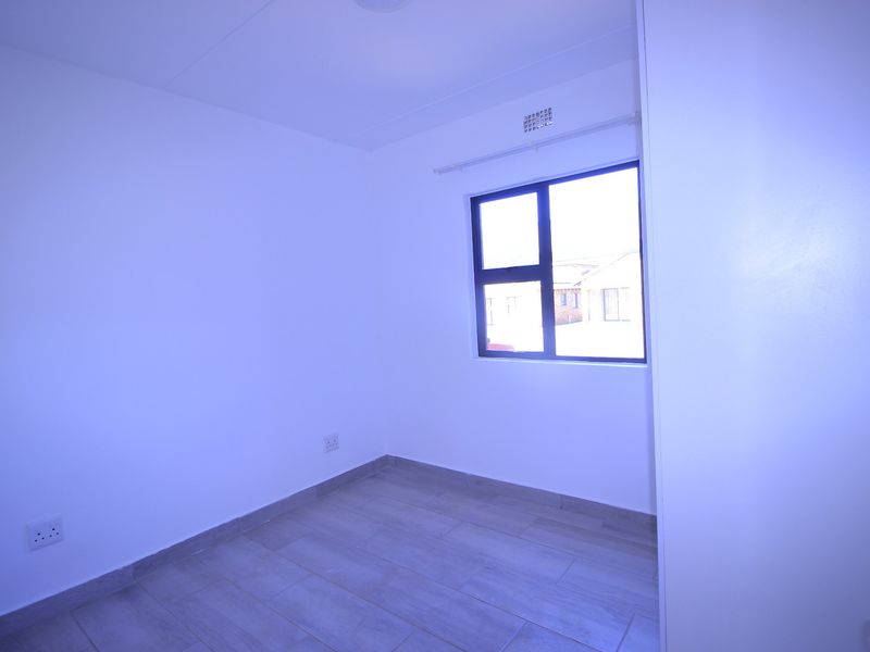 A clean, empty bedroom featuring neutral tiled flooring and a modern aluminium window frame, providing a blank canvas for personalization.