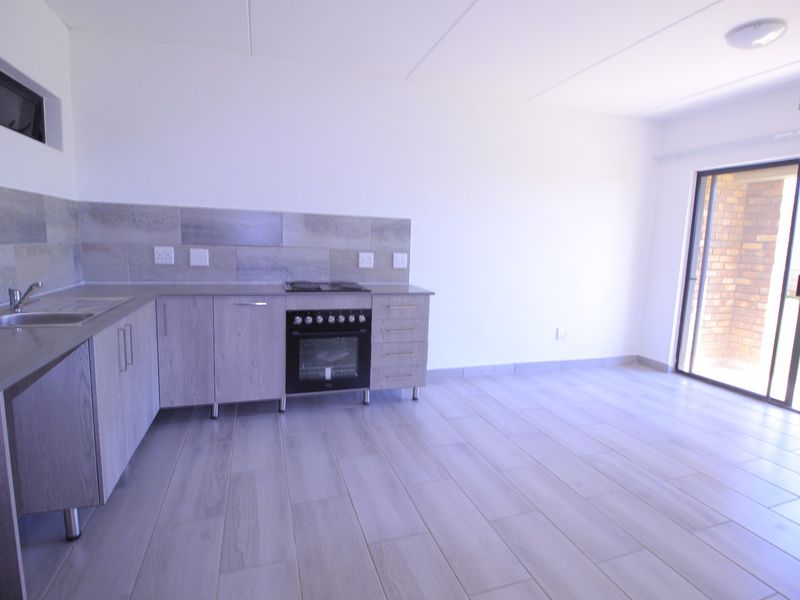 An open-plan kitchen and living area featuring modern light wood cabinetry, built-in oven, tiled splashback, and direct access to an outdoor space via sliding doors.