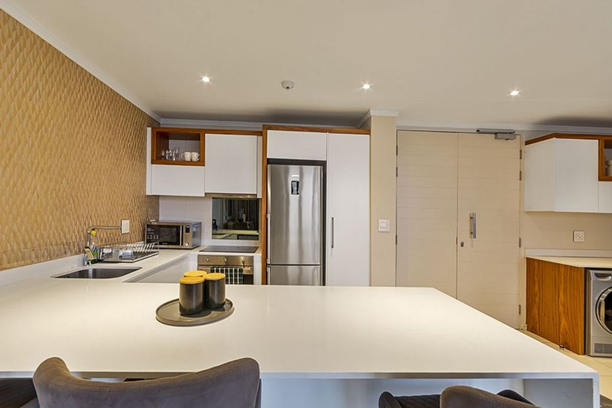 Modern kitchen featuring sleek white cabinetry, stone countertops, integrated appliances, and a textured feature wall, providing a clean and functional culinary space.