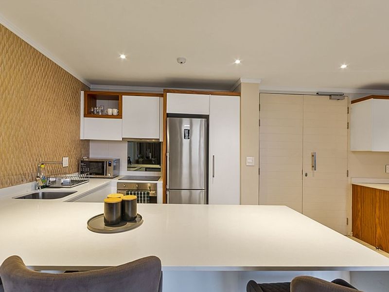Modern kitchen featuring sleek white cabinetry, stone countertops, integrated appliances, and a textured feature wall, providing a clean and functional culinary space.