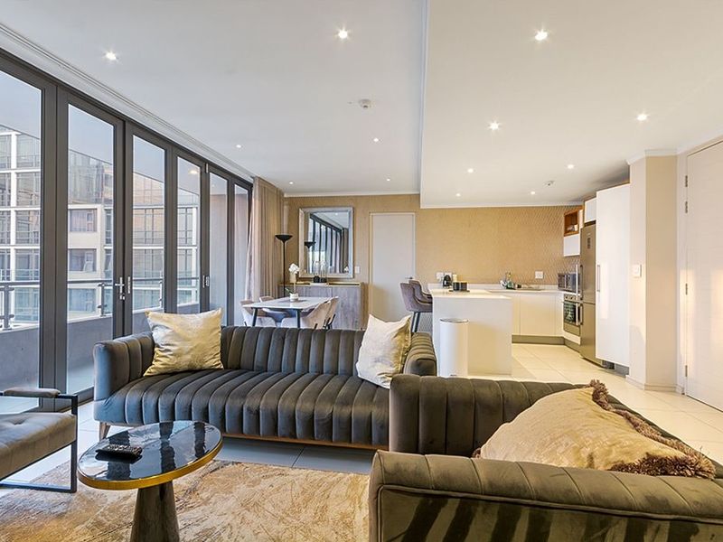 Modern open-plan living area featuring a sleek kitchen with island, tiled floors, and expansive sliding glass doors leading to a private balcony.