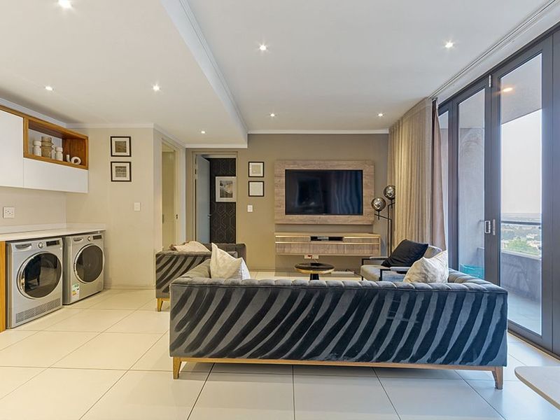 Modern open-plan living area featuring tiled floors, recessed lighting, built-in cabinetry, and large sliding doors leading to a balcony with expansive views.