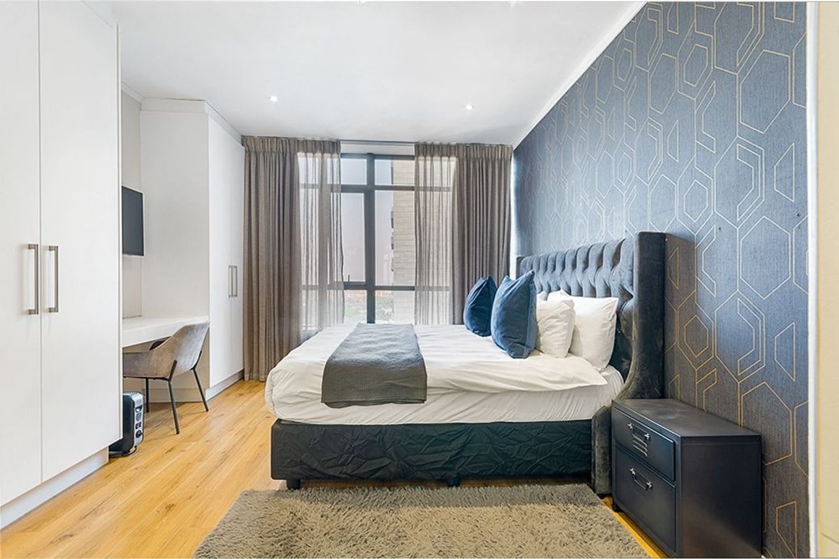 A well-maintained bedroom featuring hardwood flooring, built-in cupboards, and a large window that allows for natural light.