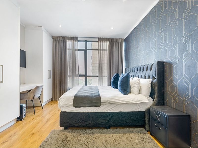 A well-maintained bedroom featuring hardwood flooring, built-in cupboards, and a large window that allows for natural light.