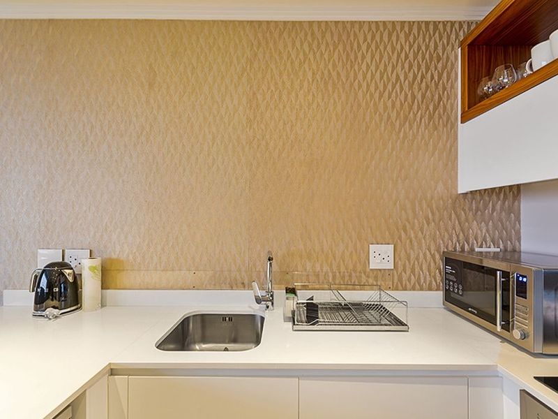 A compact kitchen area featuring white cabinetry, stone countertops, a stainless steel sink, and a distinctive textured feature wall.