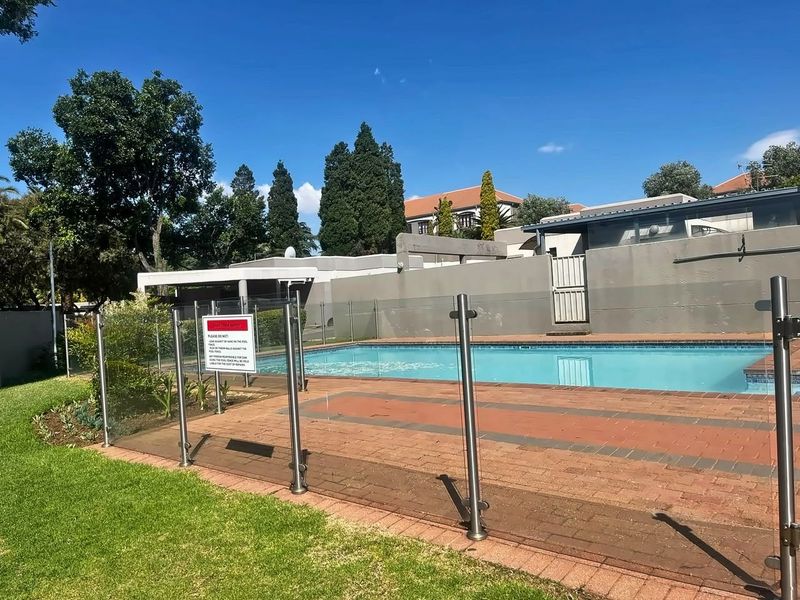 Outdoor swimming pool area featuring glass safety fencing, brick paved surround, and established garden borders.