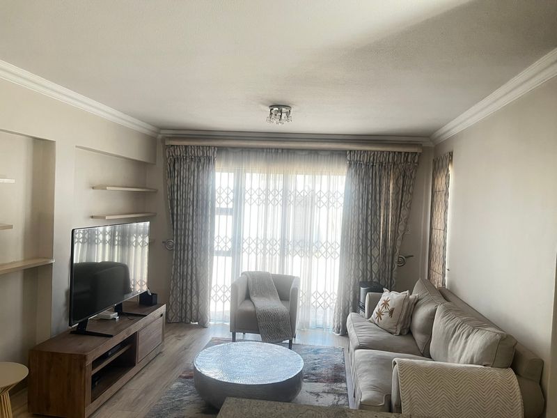A comfortable living room featuring laminate flooring, built-in wall shelving, and a sliding glass door with security gate leading to the exterior.