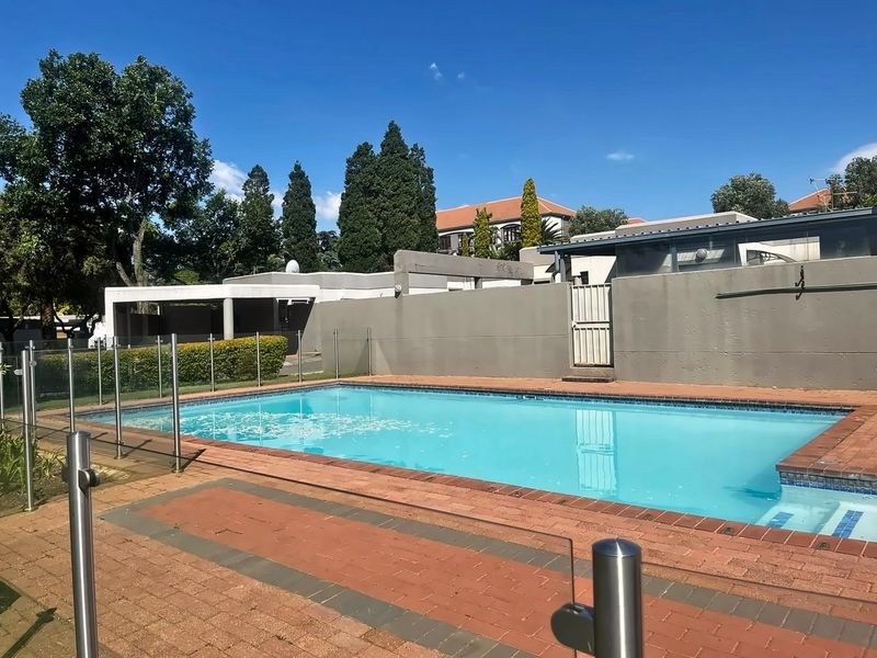 A well-maintained outdoor swimming pool area featuring brick paving, glass safety fencing, and a secure boundary wall.
