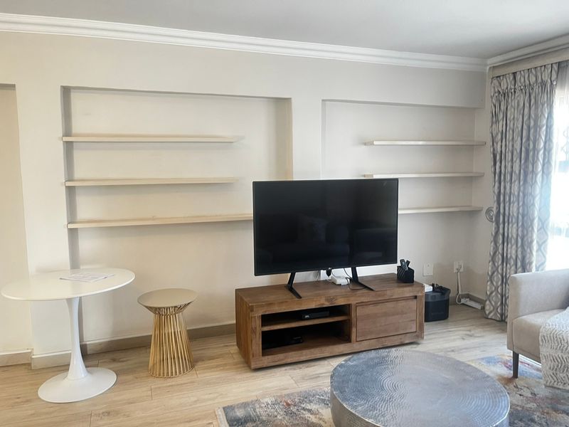 A living room featuring built-in wall shelving, crown molding, and light-toned laminate flooring, providing a clean and functional space.