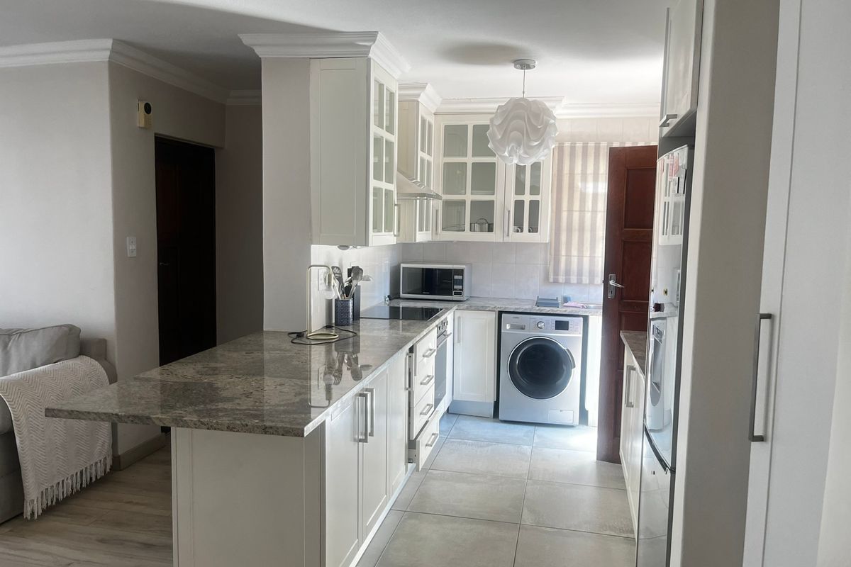 A well-maintained kitchen featuring white cabinetry, granite countertops, integrated appliances, and tiled flooring, seamlessly connected to the living area.