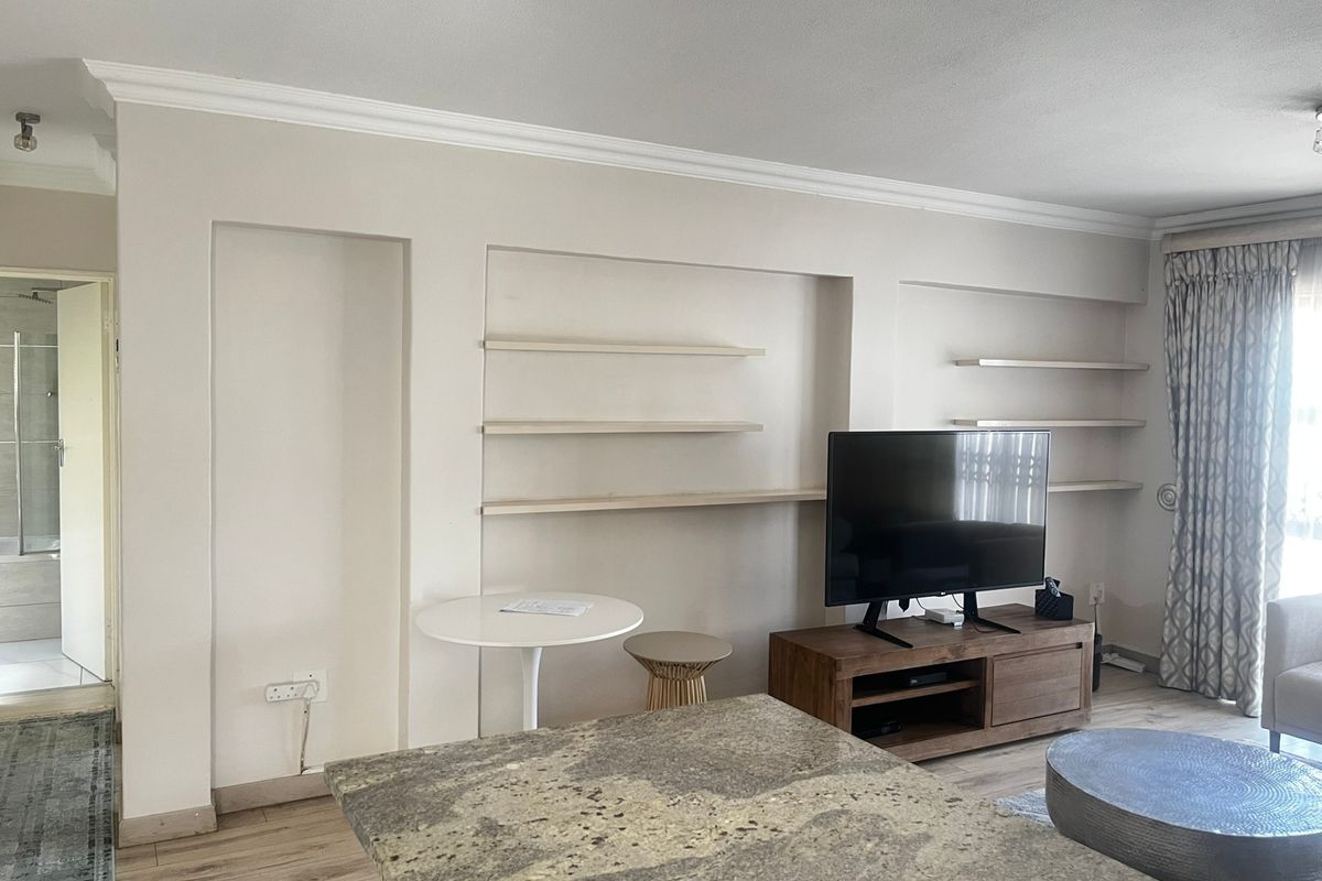 Living room featuring built-in wall shelving, laminate flooring, and decorative cove cornicing, providing a functional space with potential for modern updates.