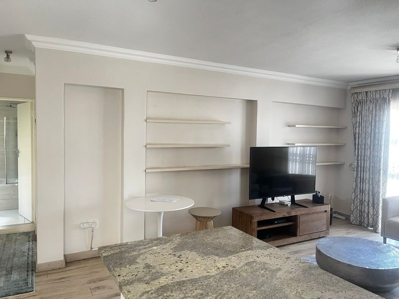 Living room featuring built-in wall shelving, laminate flooring, and decorative cove cornicing, providing a functional space with potential for modern updates.