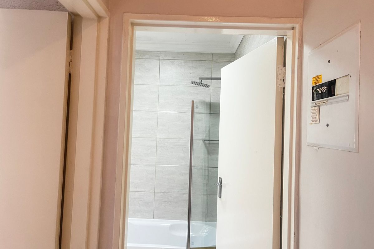 A view through a doorway into a bathroom featuring a bathtub with a glass shower screen and tiled walls.