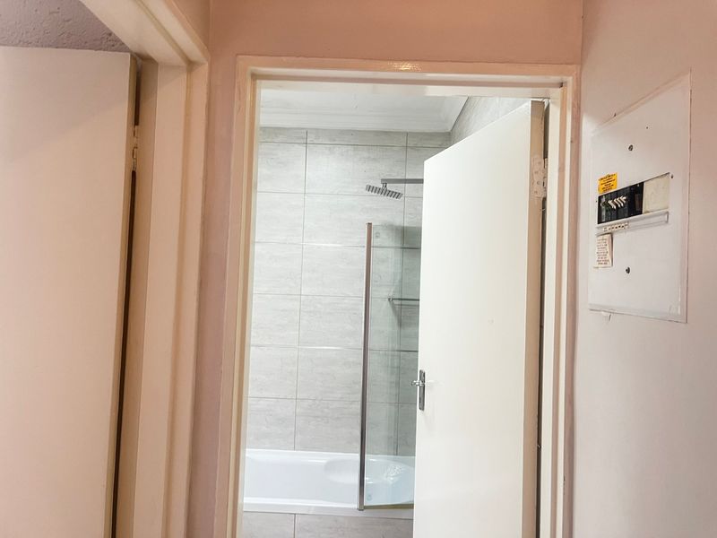 A view through a doorway into a bathroom featuring a bathtub with a glass shower screen and tiled walls.