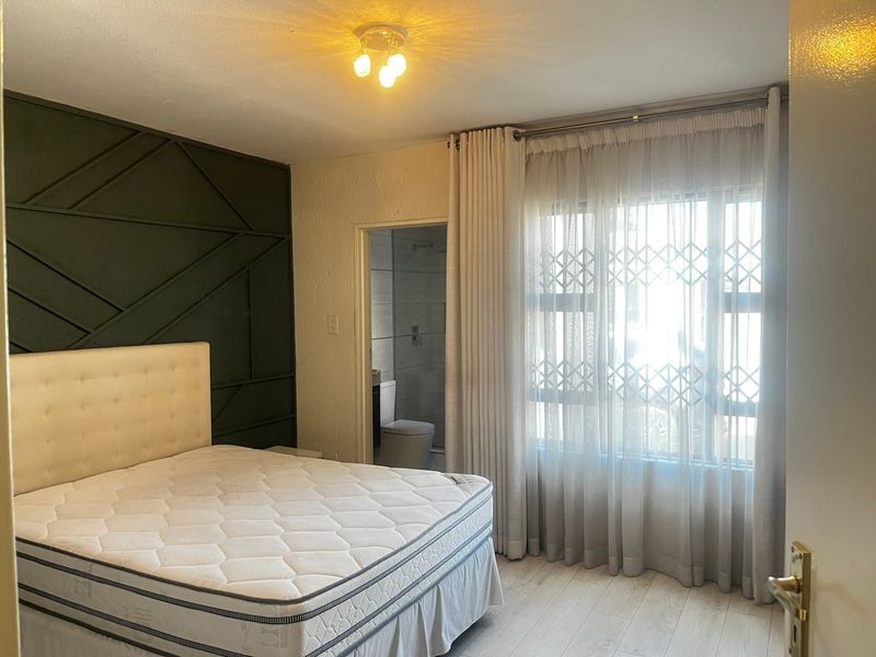 A well-lit bedroom featuring modern decorative wall paneling, light laminate flooring, and direct access to an en-suite bathroom.