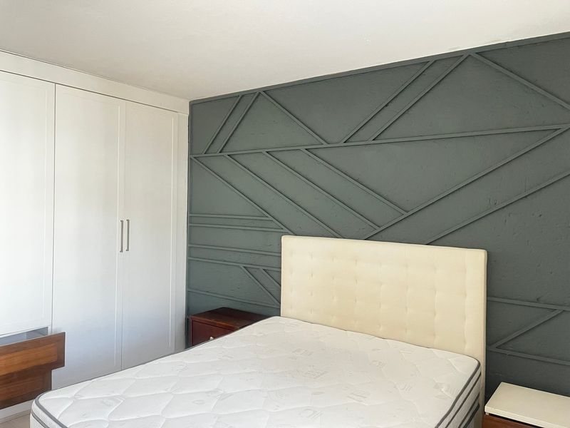 A well-maintained bedroom featuring a modern dark grey geometric feature wall and integrated white built-in wardrobes.